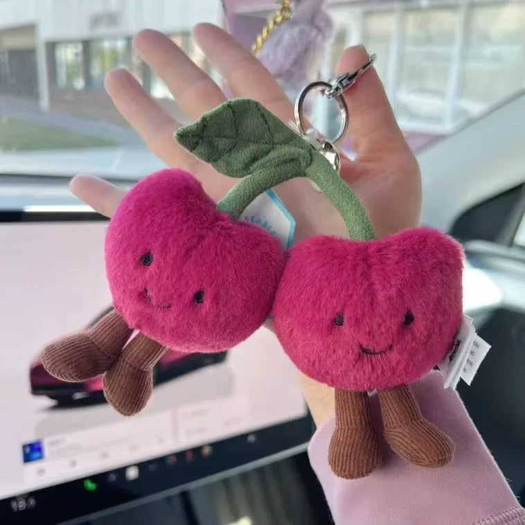 Two plush heart-shaped keychains with faces held in a hand, with a car interior in the background.